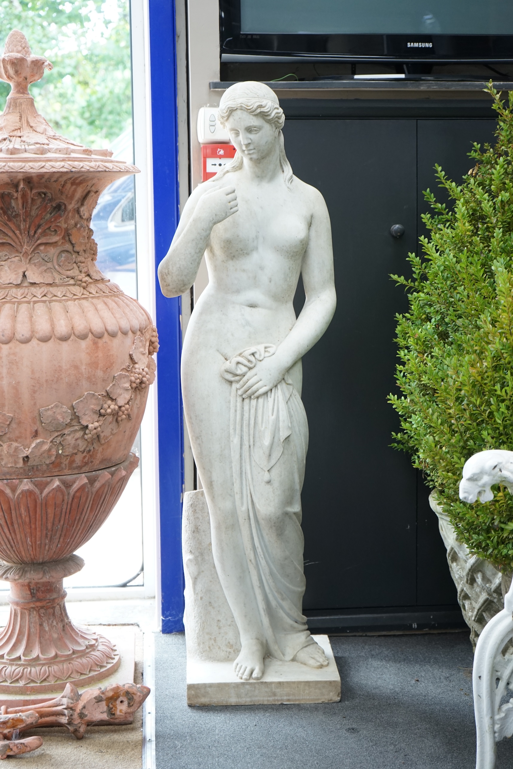 After the Antique. A large carved reconstituted marble figure of Venus, standing beside a tree trunk, 141cm high